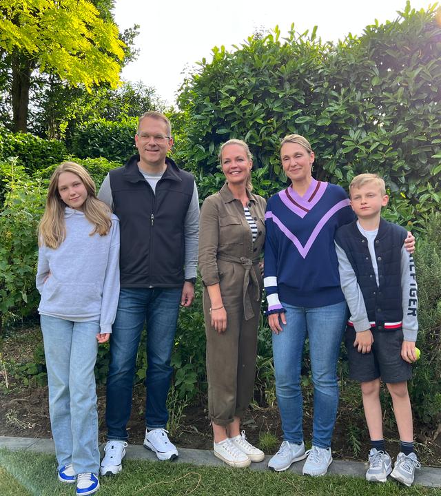 Familie Kossey stehen mit Eva Brenner vor einer Hecke und lächeln in die Kamera.