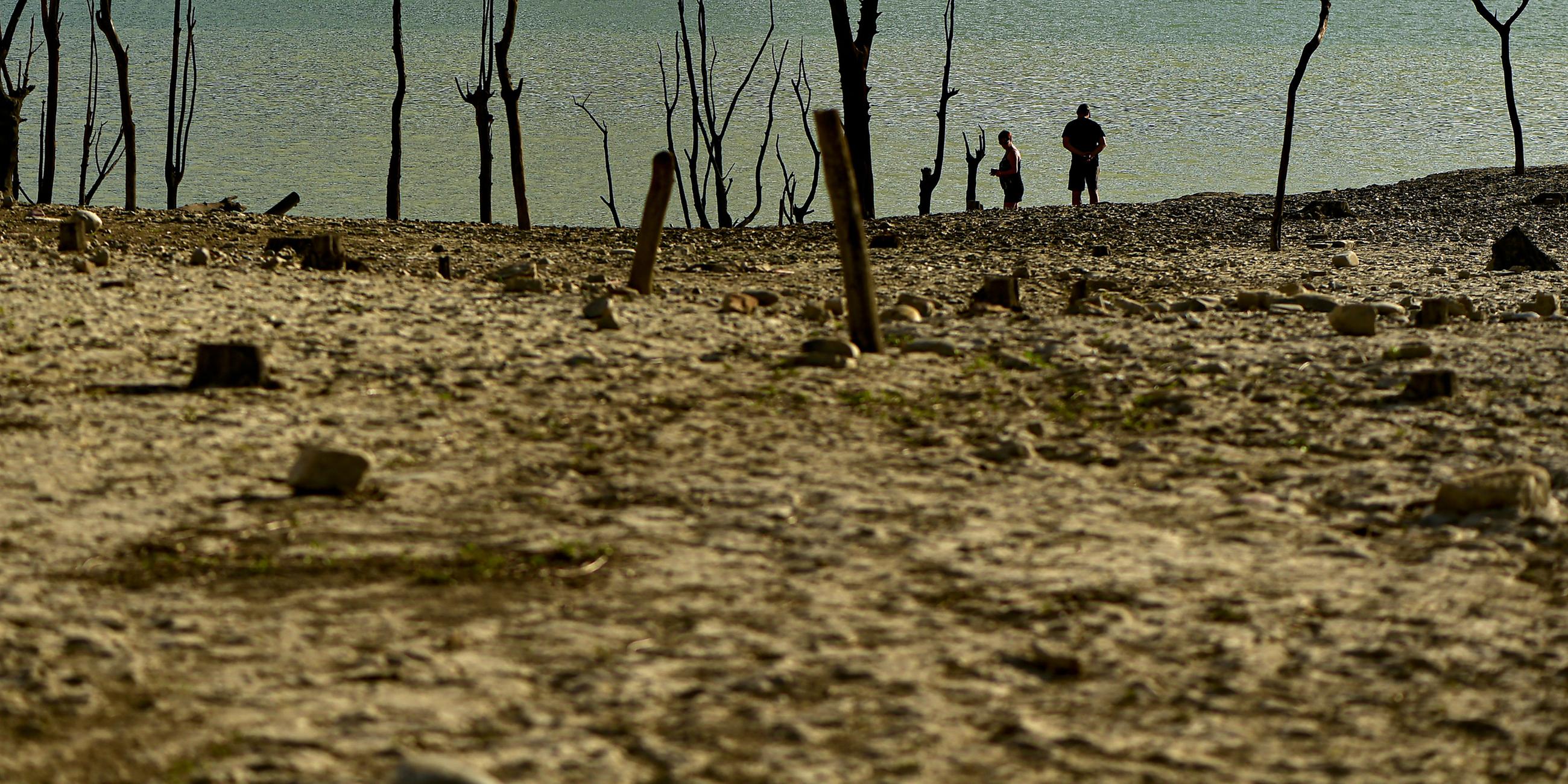 Menschen spazieren an einem sonnigen Sommertag am Ufer des von der Dürre betroffenen Yesa-Stausees in Nordspanien entlang.