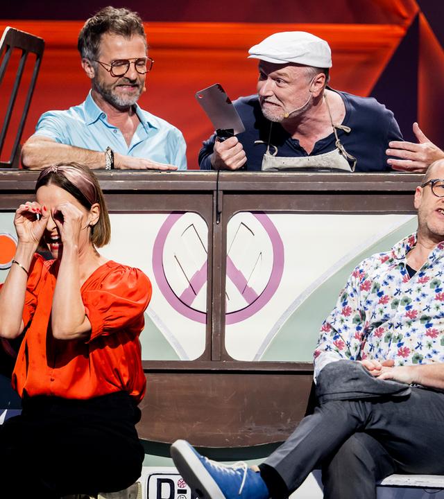 Das Ensemble des Düsseldorfer Kom(m)ödchens ist auf der Bühne zu sehen. Im Hintergrund ist ein Bus. Die Bühne ist rot beleuchtet.