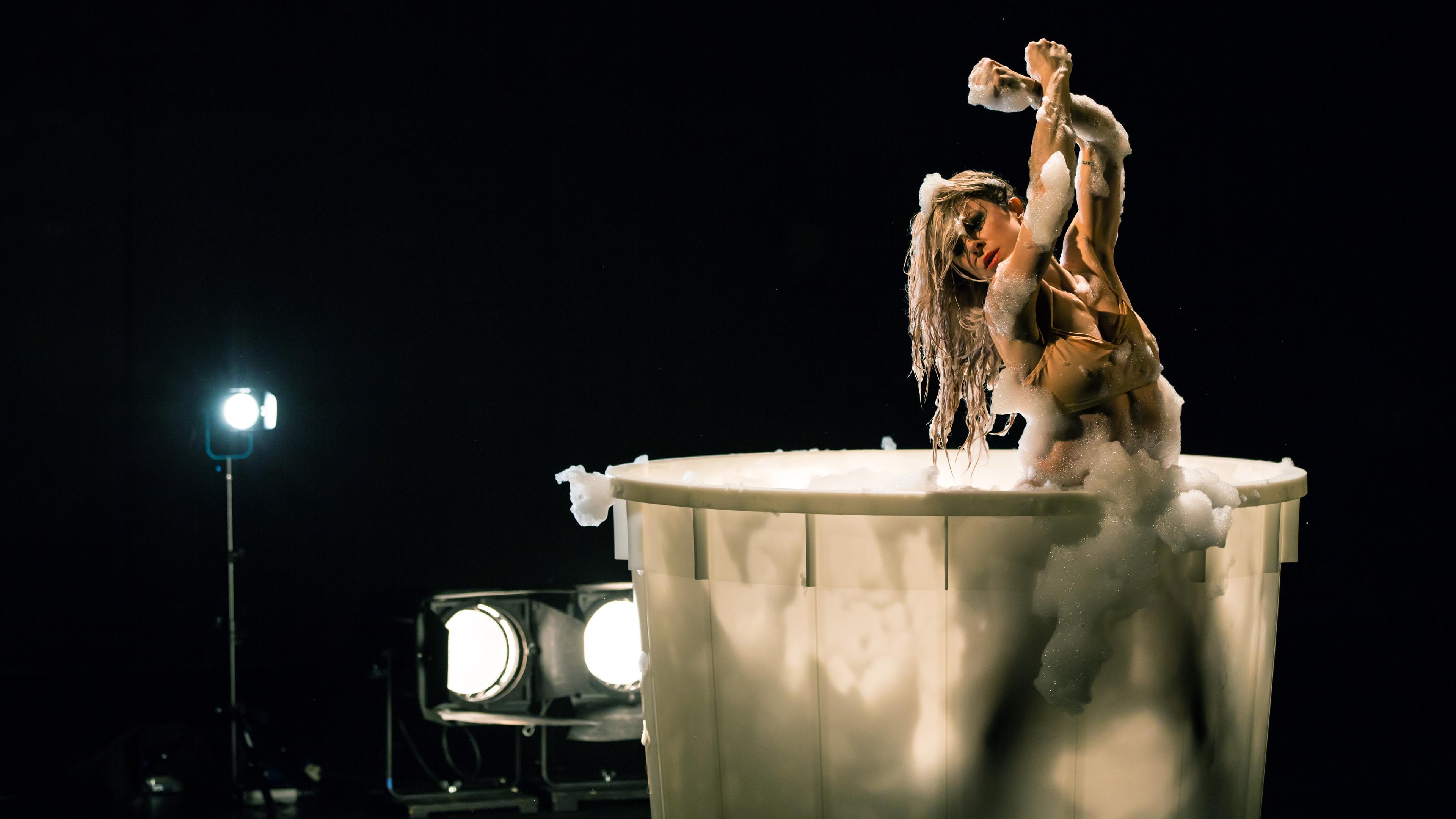 Tänzerin Garazi Perez Oloriz steht in einer mit Schaum gefüllten Plastikwanne, mal den Kopf nach vorne geneigt, mal die Hände nach oben gestreckt. Dabei bedeckt der Schaum teilweise ihren Körper.