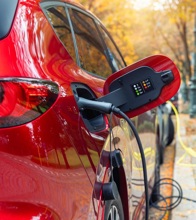Ein Elektroauto steht am Straßenrand und wird über eine öffentliche Ladesäule geladen. Mehrere Kabel liegen am Boden, während im Hintergrund weitere Ladepunkte und parkende Autos zu sehen sind. Das Bild macht sichtbar, dass ohne eigene Wallbox viele Mieter auf öffentliche Lademöglichkeiten angewiesen sind.