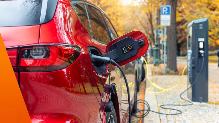 Ein Elektroauto steht am Straßenrand und wird über eine öffentliche Ladesäule geladen. Mehrere Kabel liegen am Boden, während im Hintergrund weitere Ladepunkte und parkende Autos zu sehen sind. Das Bild macht sichtbar, dass ohne eigene Wallbox viele Mieter auf öffentliche Lademöglichkeiten angewiesen sind.
