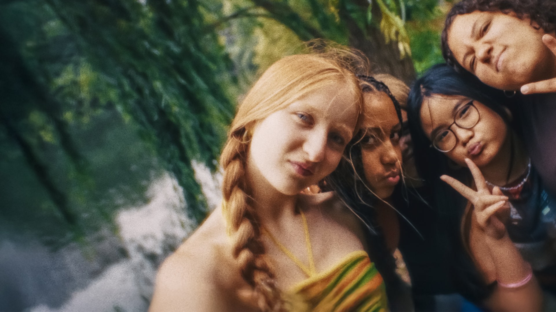 Ein Selfie zeigt Paula, Milli, Châo und Samira, die, ihre Köpfe aneinandergelehnt, gut gelaunt in die Kamera schauen. Châo und Samira machen ein Victory-Zeichen. Im Hintergrund sind Bäume und Wasser zu sehen.