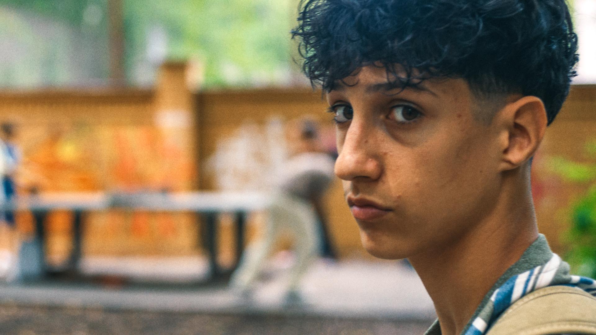 Pit ist auf dem Schulhof und schaut nachdenklich in die Kamera. Im Hintergrund ist die Tischtennisplatte mit zwei Spielern zu sehen.