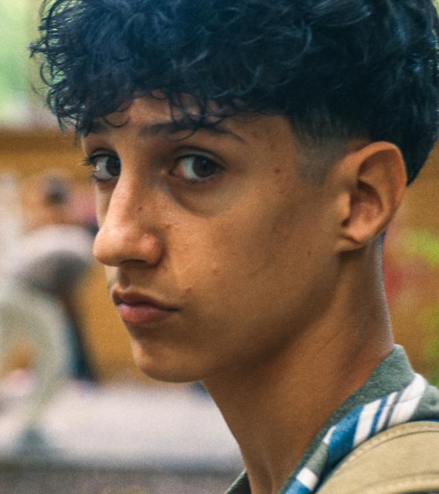 Pit ist auf dem Schulhof und schaut nachdenklich in die Kamera. Im Hintergrund ist die Tischtennisplatte mit zwei Spielern zu sehen.