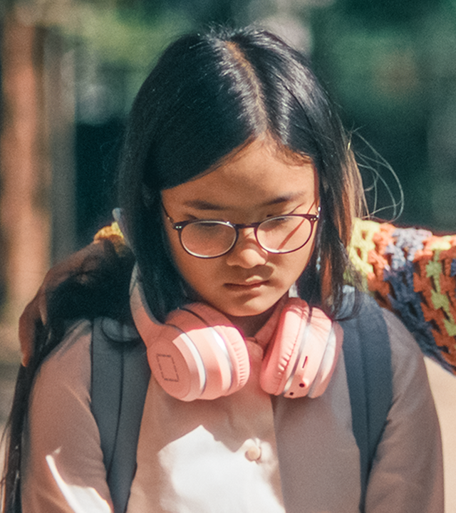 Auf dem Schulhof stehen Châu und Milli nah nebeneinander. Châu lässt traurig den Kopf hängen, und Milli schaut betroffen zu ihrer Freundin und hat ihren rechten Arm um deren Schultern gelegt.