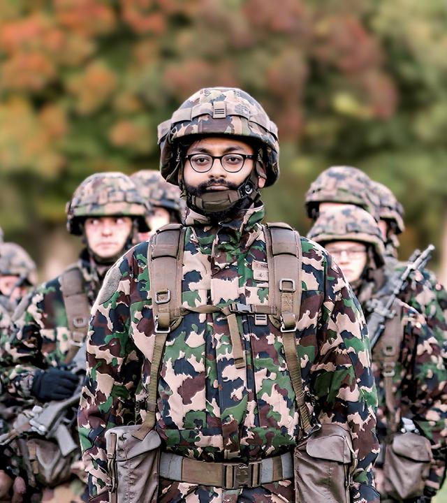 Eine Gruppe von Soldaten in Tarnuniform steht in Formation im Freien, im Vordergrund ein Soldat mit Brille und Bart.