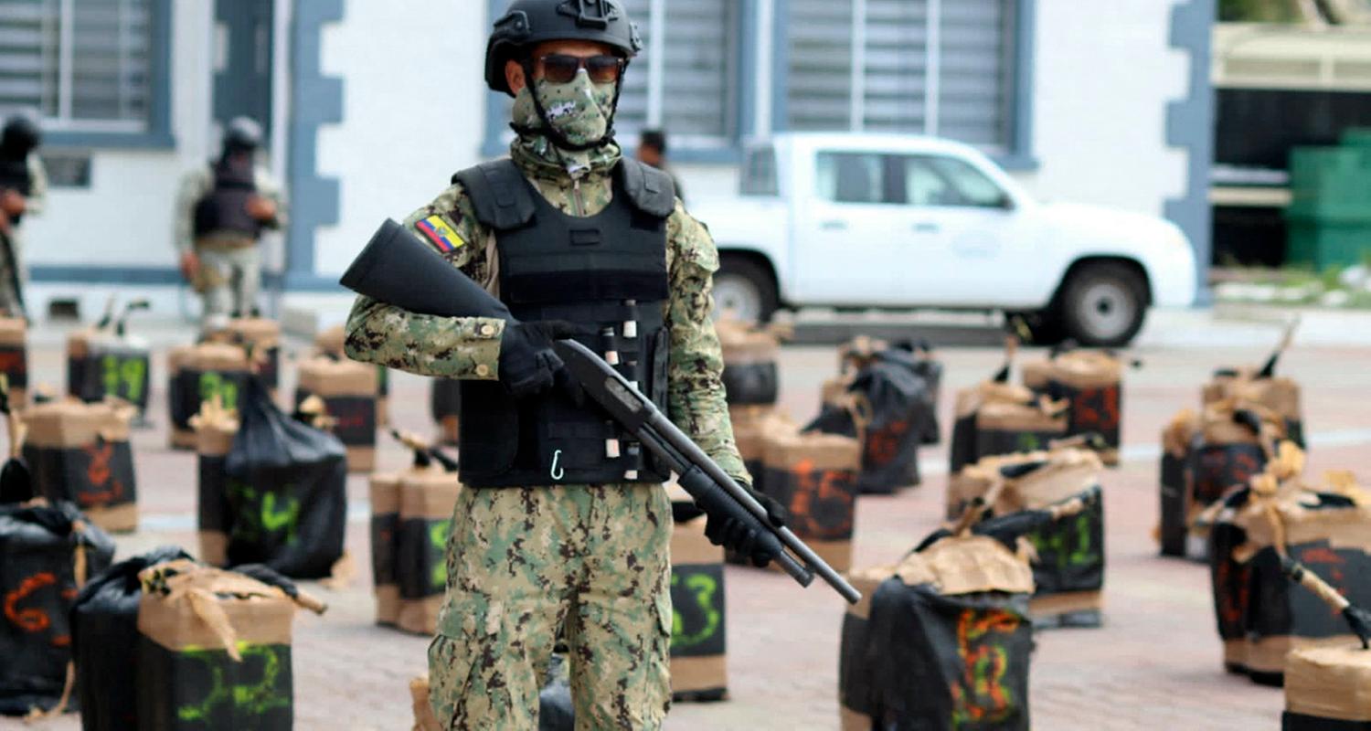 Ein bewaffneter Soldat steht vor beschlagnahmten Drogenpaketen.