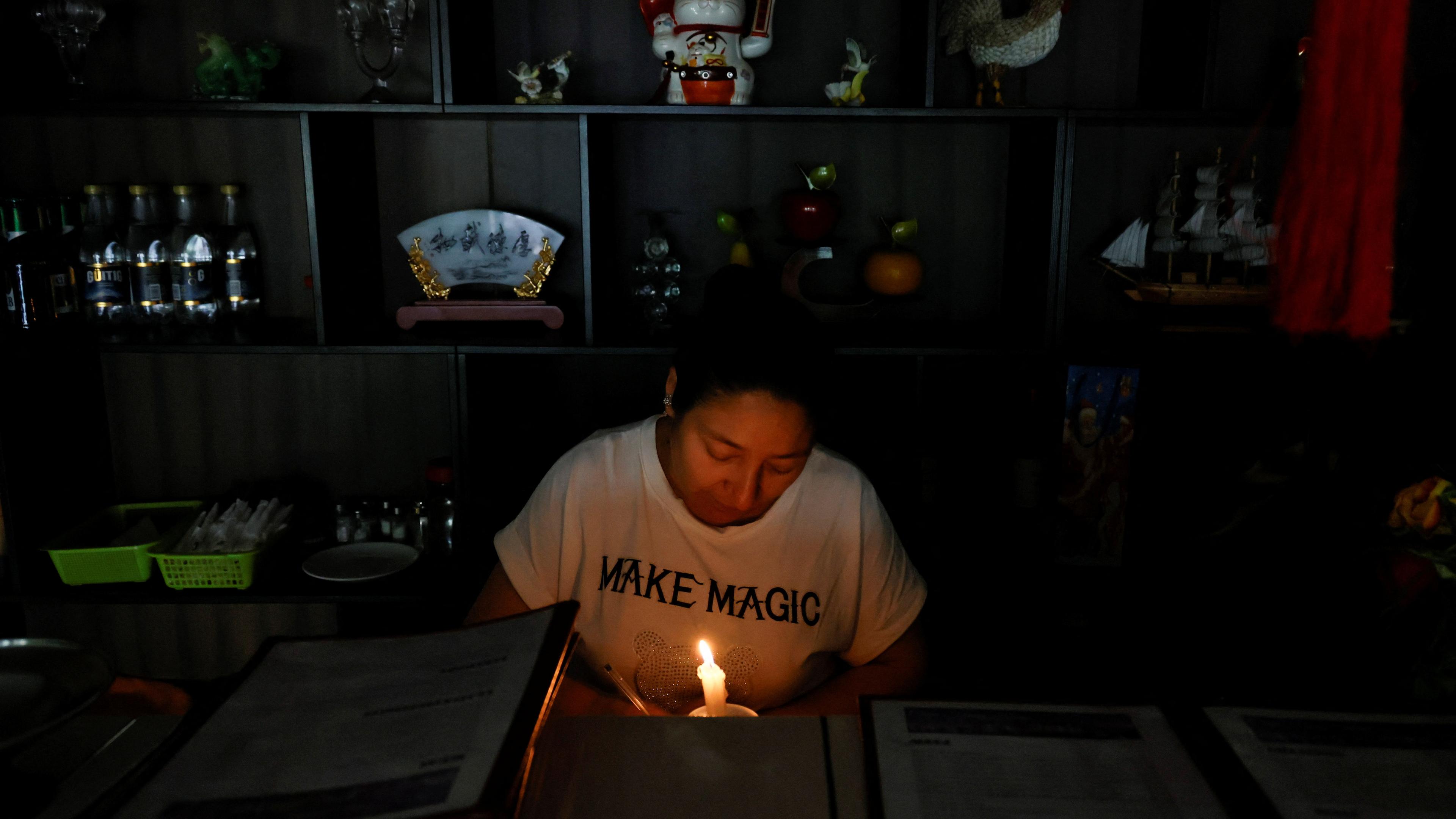 Eine Ladenbesitzerin sitzt in einem dunklen Laden mit einer Kerze