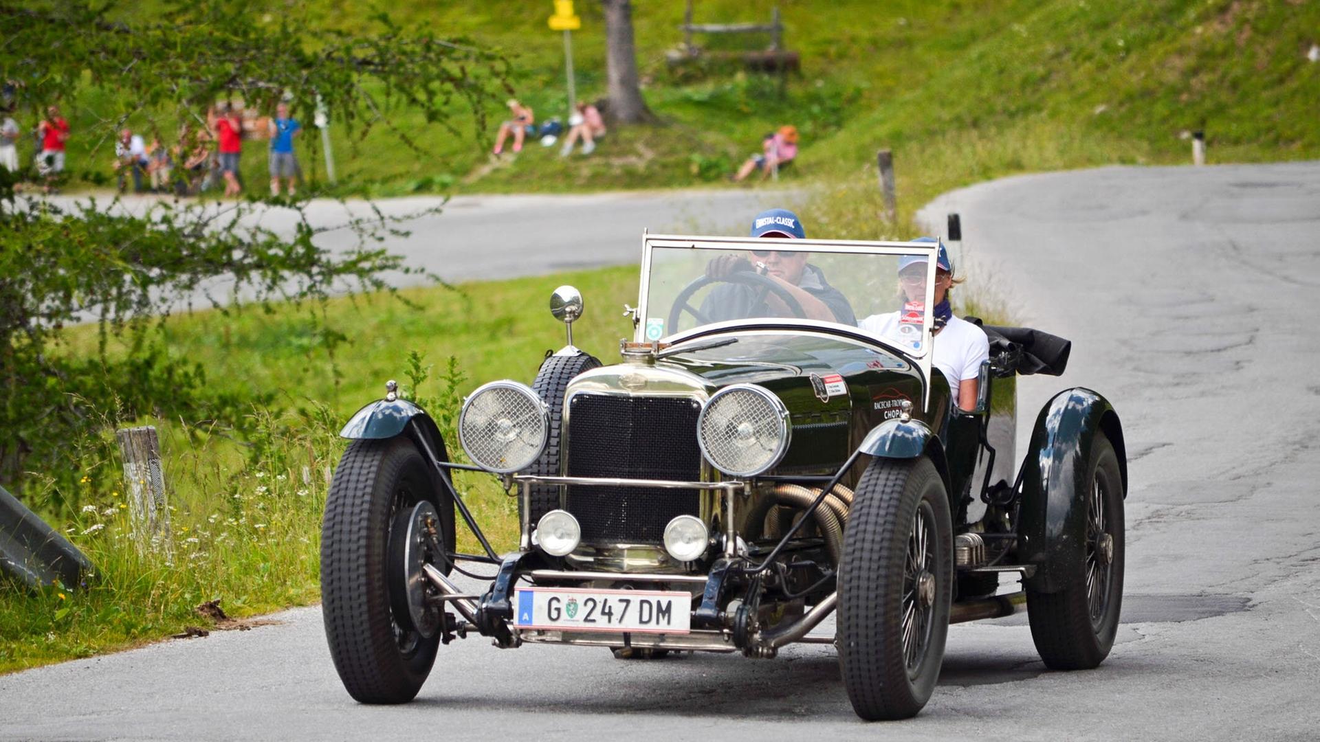 Ein dunkelgrüner Sunbeam Supersport Oldtimer mit zwei Insassen fährt eine Bergstraße entlang, im Hintergrund Zuschauer auf einer Wiese.