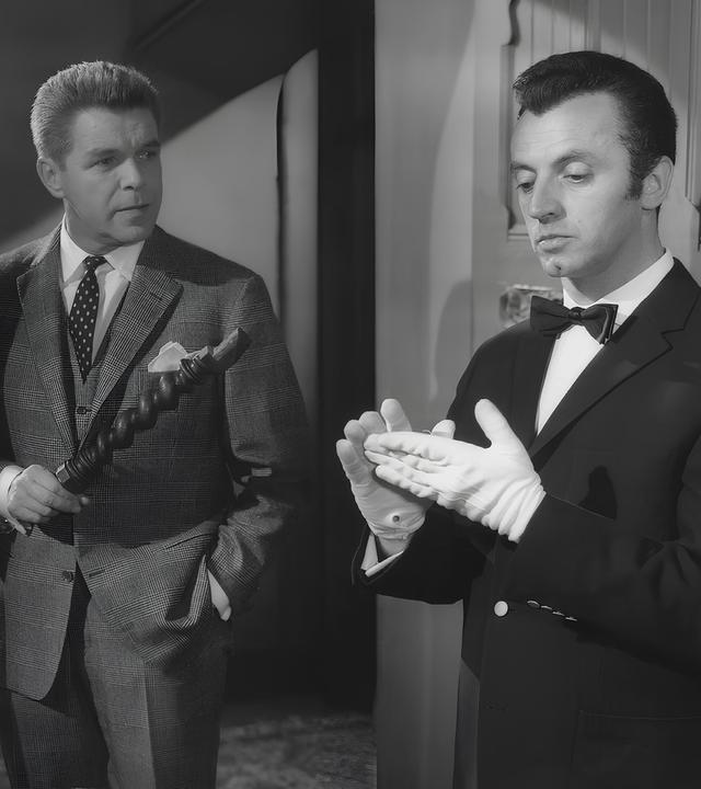 Frank Tanner (Heinz Drache) schaut erstaunt zu Butler Bonwit, der weiße Handschuhe trägt und sich die Hände abwischt.