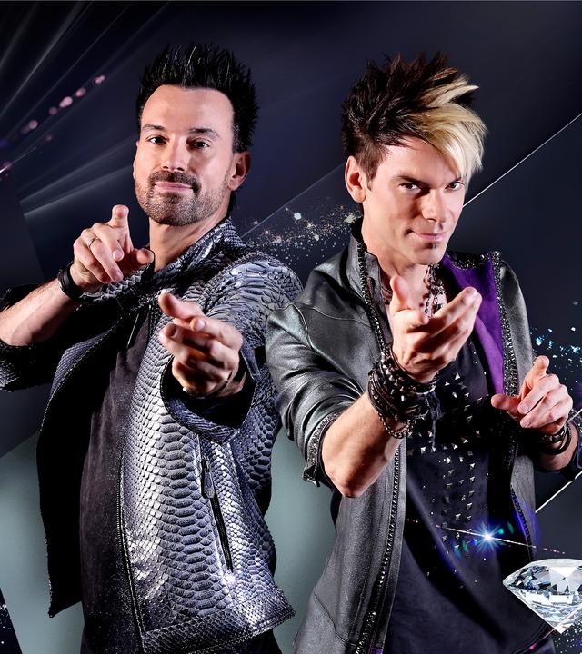 Am linken Bildrand sind die Ehrlich Brothers zu sehen (links Andreas Ehrlich, rechts Chris Ehrlich). Sie lächeln in die Kamera und formen mit ihren Händen einladende Show-Gesten. Im Hintergrund sind stilisierte Diamanten, Glitzer und Reflektionen zu sehen.