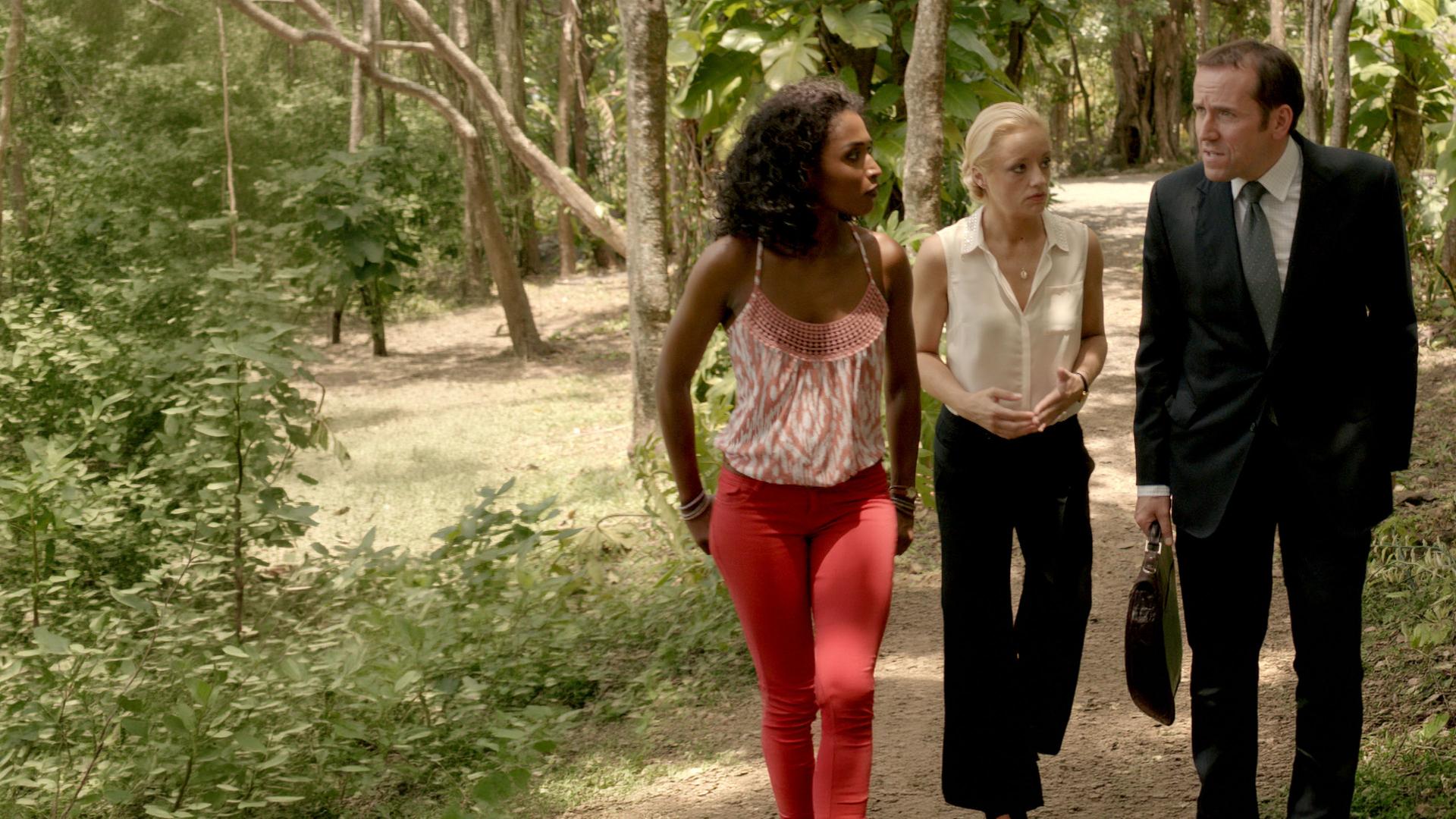 "Death in Paradise - Ein (fast) perfekter Plan": Camille Bordey (Sara Martins), Vicky Woodward (Lucy Davis) schauen gespannt DI Richard Poole (Ben Miller) an, der mit ihnen redet. Alle drei laufen nebeneinander im Freien einen Weg entlang.