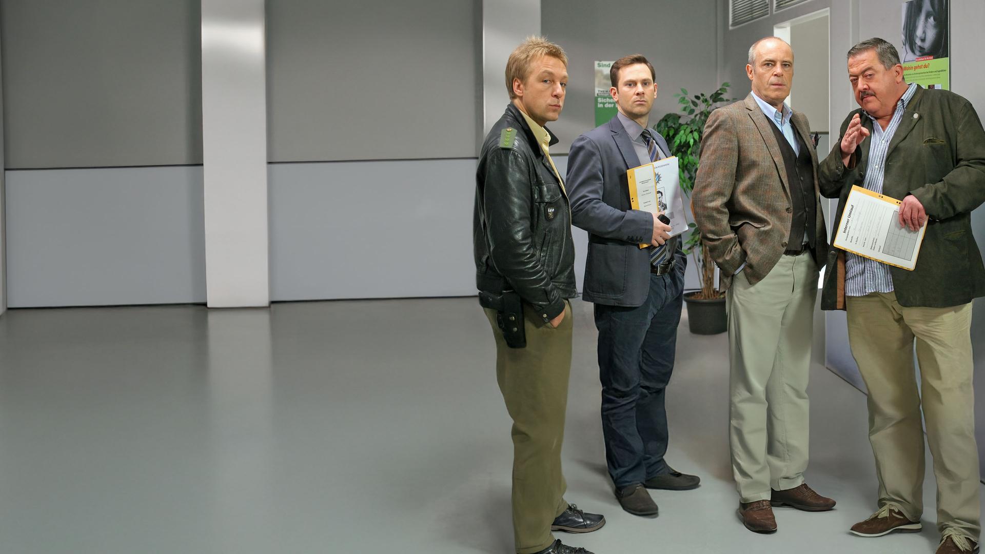 "Die Rosenheim-Cops - Ein geschätzter Schätzer": Kommissar Hofer (Joseph Hannesschläger), Kommissar König (Mark-Alexander Solf) und Polizist Mohr (Michael Müller) befragen den Musikhändler Traunstein (Peter Kremer) auf dem Gang des Kommissariats.