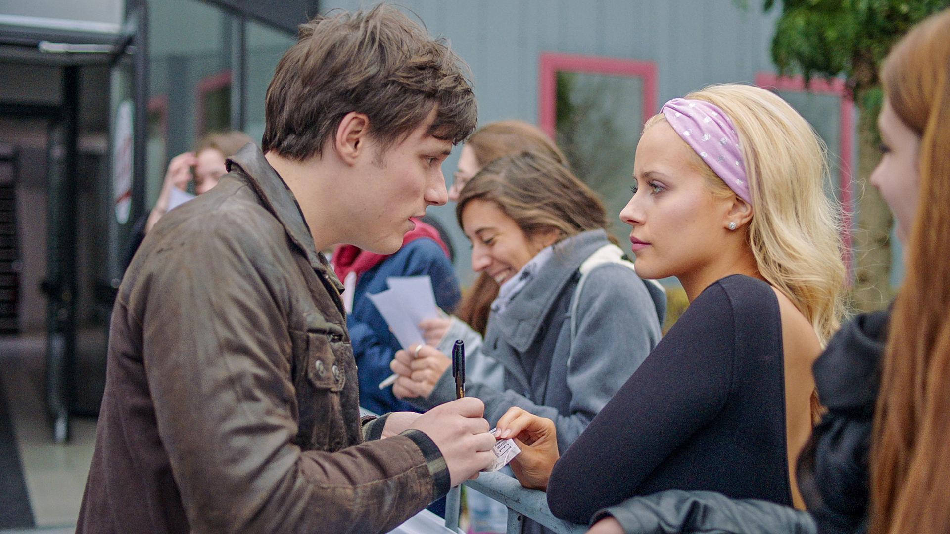 Lena steht mit Henris Fans am Radiosender. Henri unterschreibt eine Autogrammkarte für sie. Lena wirkt wütend.
