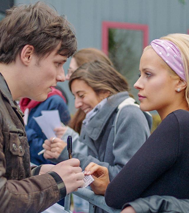 Lena steht mit Henris Fans am Radiosender. Henri unterschreibt eine Autogrammkarte für sie. Lena wirkt wütend.