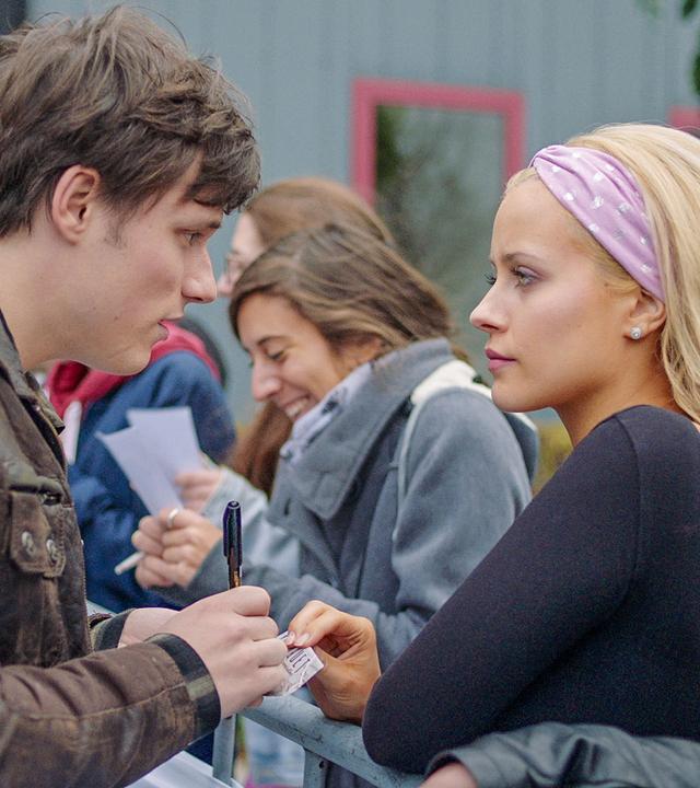 Lena steht mit Henris Fans am Radiosender. Henri unterschreibt eine Autogrammkarte für sie. Lena wirkt wütend.