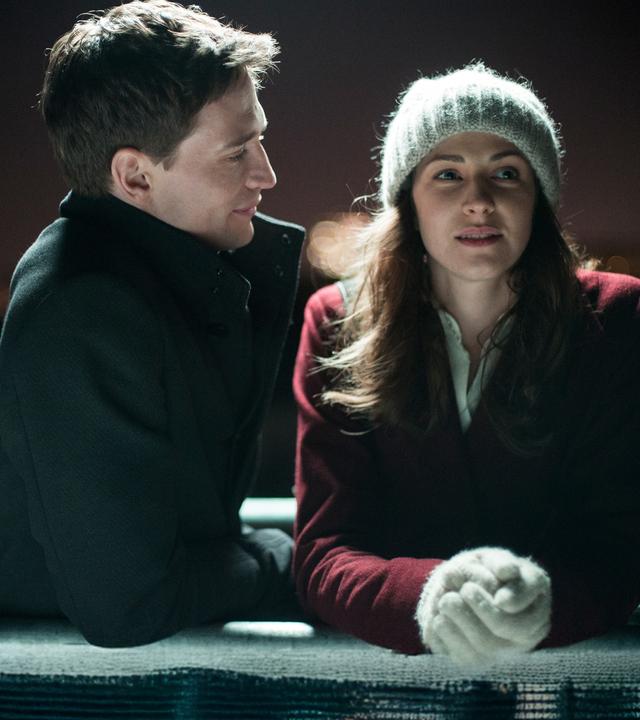 "Ein Lächeln nachts um vier": Max (August Wittgenstein) und Jule (Natalia Belitski) stehen bei Nacht draußen und lehnen sich auf ein Geländer. Sie sind winterlich gekleidet.