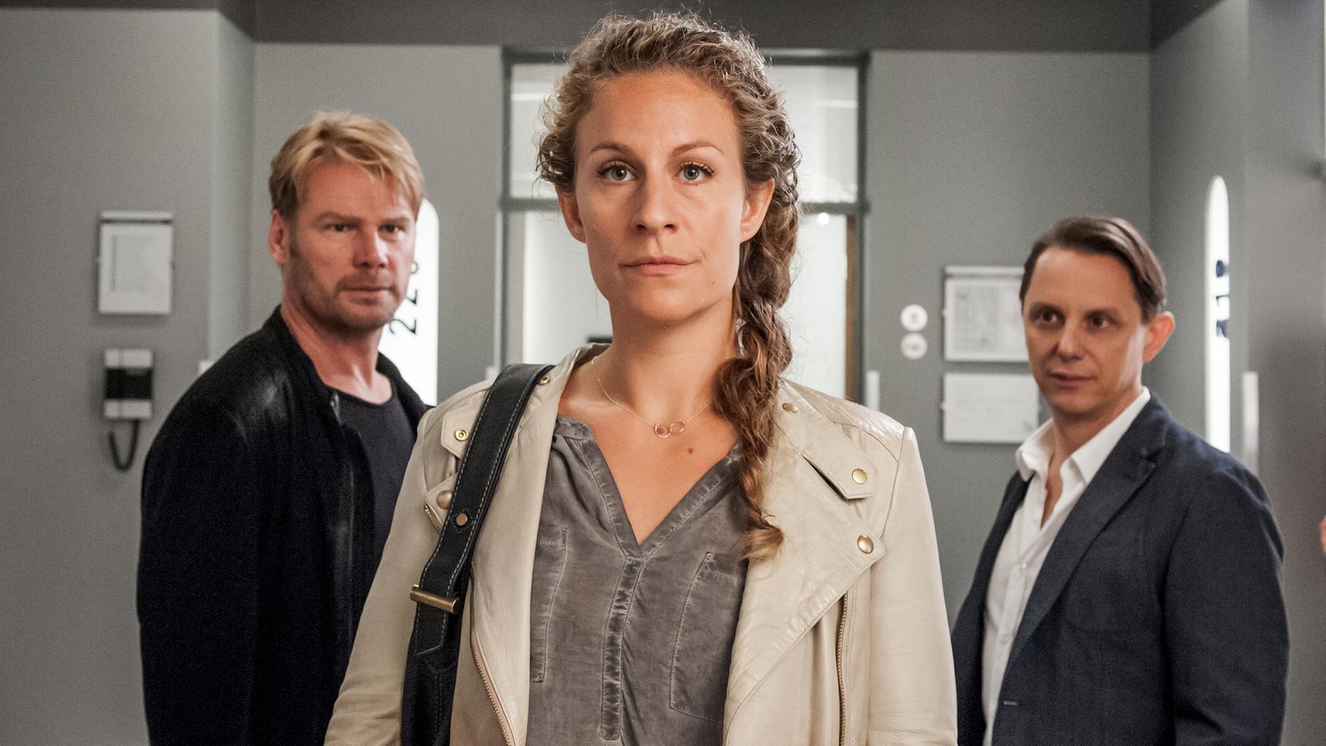 "Der Bergdoktor - Ein letztes Lied (2)": Robert Selig (Kai Scheve) und Lenni Rödel (Arndt Schwering-Sohnrey) stehen im Gang und betrachten Katharina Selig (Alessija Lause), die ihnen den Rücken zukehrt.