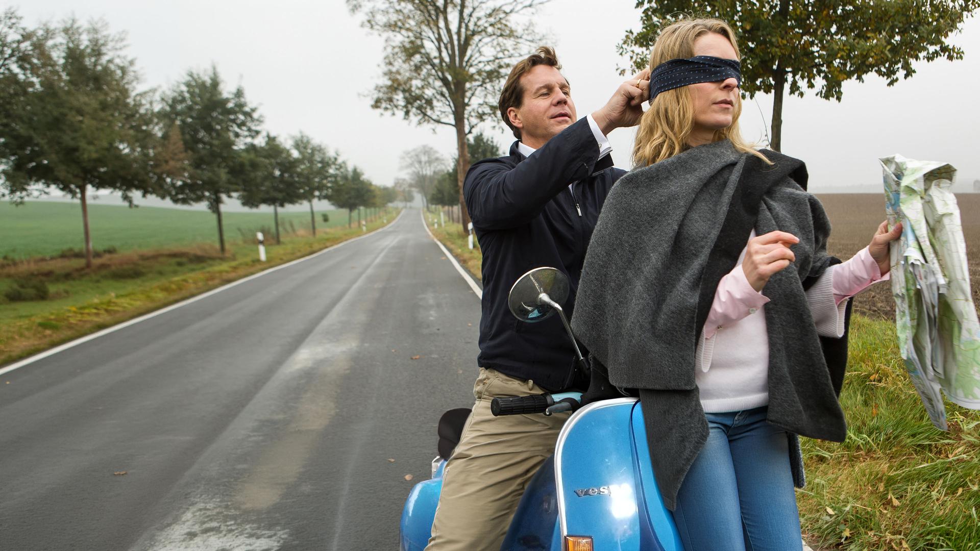 Rainer (Thomas Heinze) sitzt auf einem Motorroller und bindet Eva (Lisa Martinek) eine Augenbinde um.