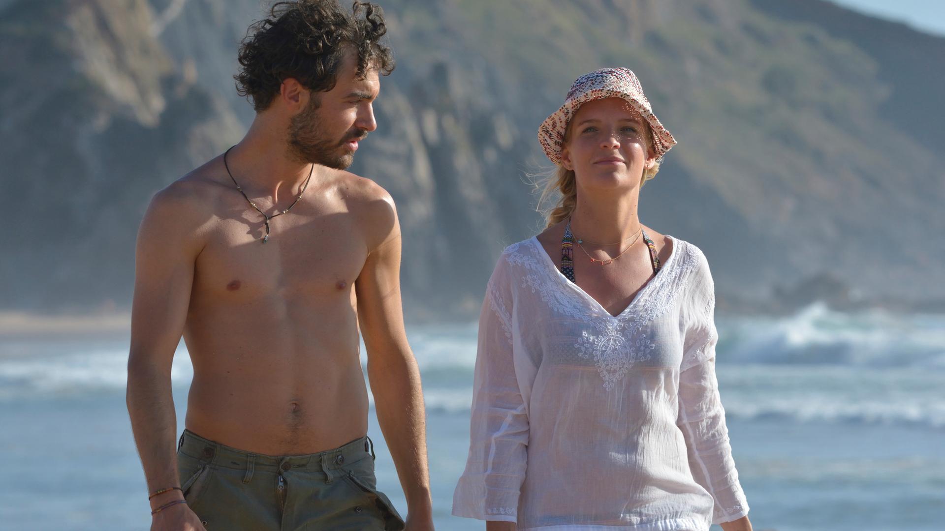 "Ein Sommer an der Algarve": An der Meeresküste laufen Miguel Silva (Giovanni Funiati) und Julika Bergmann (Bea Brocks) nebeneinander her. Er schaut zu ihr und sie schaut nach vorne.