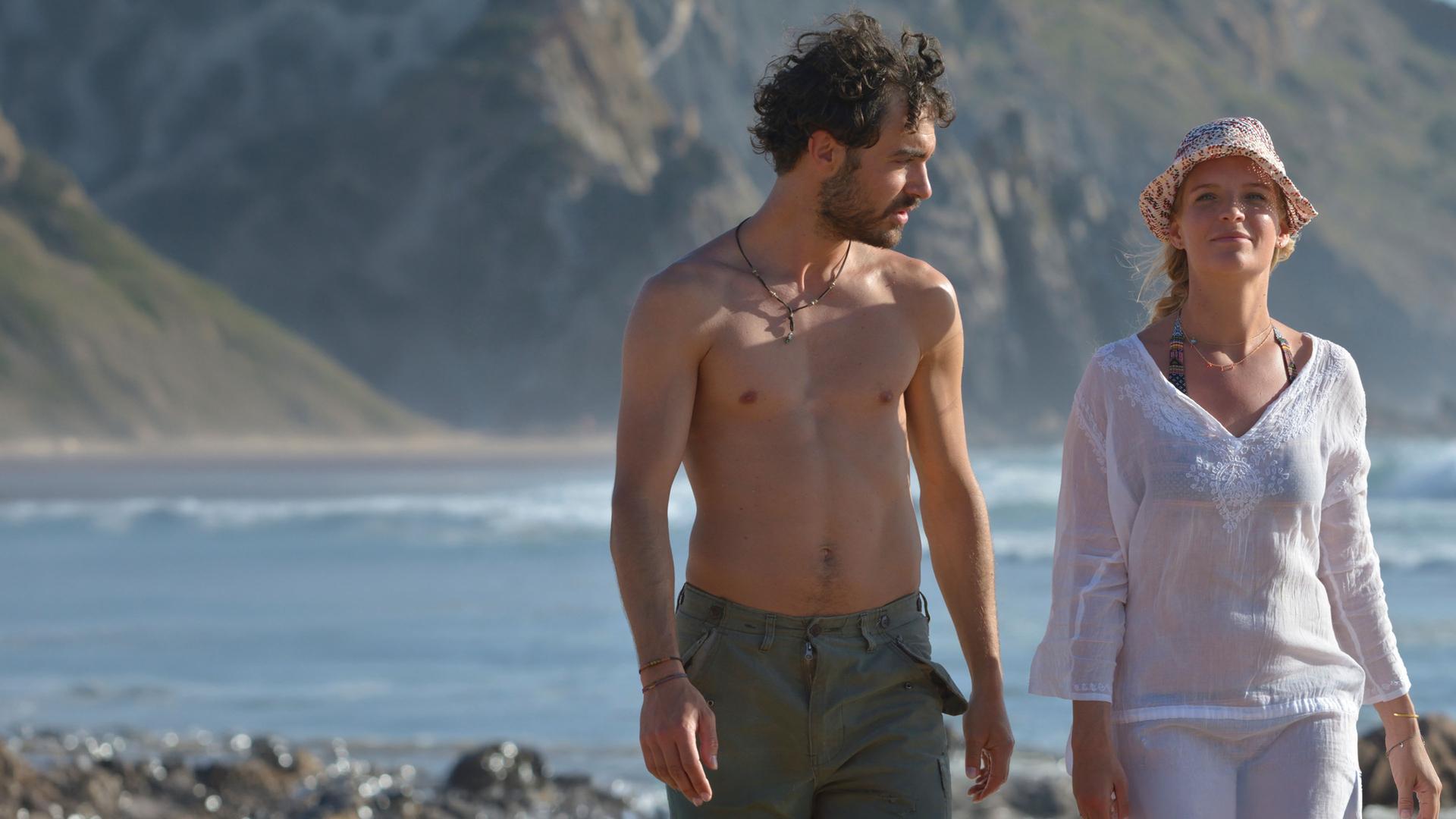 "Ein Sommer an der Algarve": An der Meeresküste laufen Miguel Silva (Giovanni Funiati) und Julika Bergmann (Bea Brocks) nebeneinander her. Er schaut zu ihr und sie schaut nach vorne.