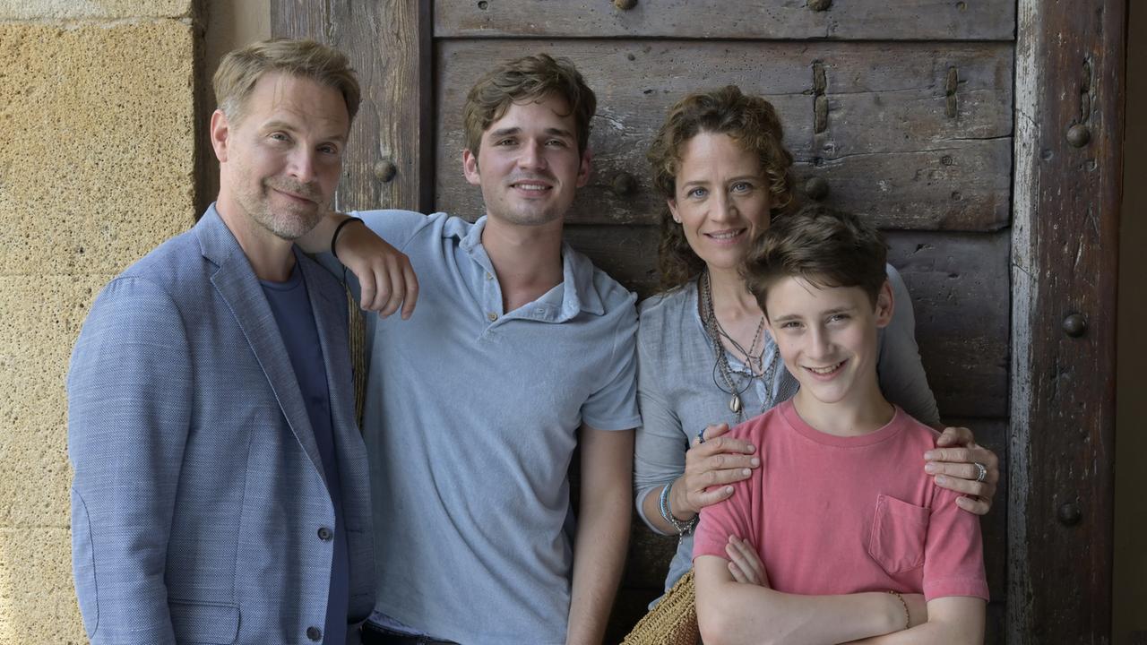 "Ein Sommer auf Elba": Vor einer dunklen Tür auf einer Terrasse steht Maja und ihre Familie. Von links: ihr Ex-Mann Thorsten (Janek Rieke), daneben ihr 17-jähriger Sohn Anton (Henry Horn). Maja (Regula Grauwiller) hat ihrem jüngeren Sohn Erik (Levis Kachel) liebevoll die Hände auf die Schultern gelegt.