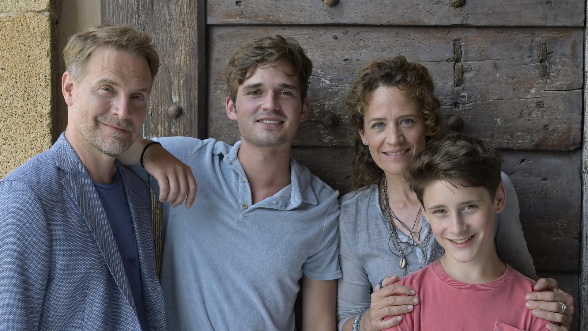 "Ein Sommer auf Elba": Vor einer dunklen Tür auf einer Terrasse steht Maja und ihre Familie. Von links: ihr Ex-Mann Thorsten (Janek Rieke), daneben ihr 17-jähriger Sohn Anton (Henry Horn). Maja (Regula Grauwiller) hat ihrem jüngeren Sohn Erik (Levis Kachel) liebevoll die Hände auf die Schultern gelegt.