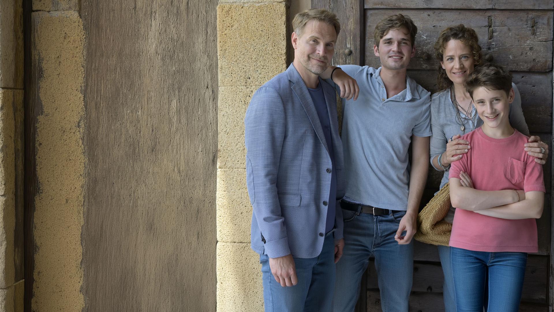 "Ein Sommer auf Elba": Vor einer dunklen Tür auf einer Terrasse steht Maja und ihre Familie. Von links: ihr Ex-Mann Thorsten (Janek Rieke), daneben ihr 17-jähriger Sohn Anton (Henry Horn). Maja (Regula Grauwiller) hat ihrem jüngeren Sohn Erik (Levis Kachel) liebevoll die Hände auf die Schultern gelegt.
