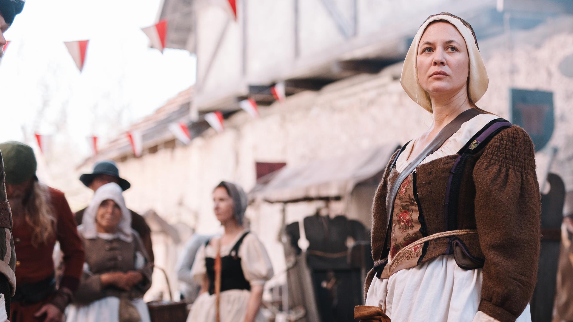 Spielszene: Hebamme Anna Stein (Julia Thurnau)  steht auf der Straße zwischen anderen Menschen