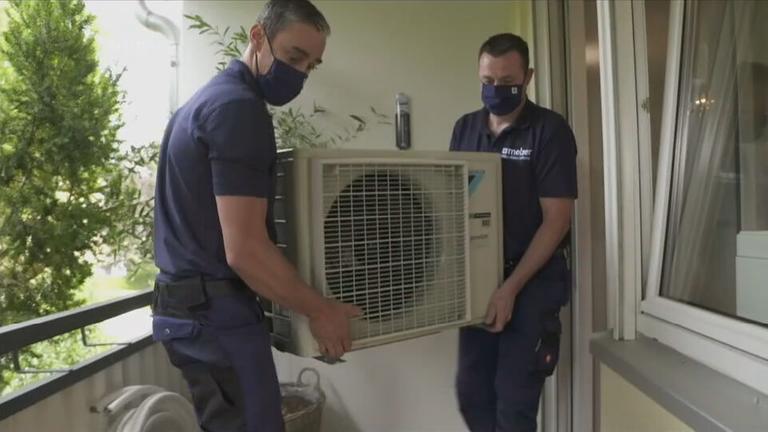 Zwei Männer tragen das Außengerät einer Klimaanlage auf einen Balkon