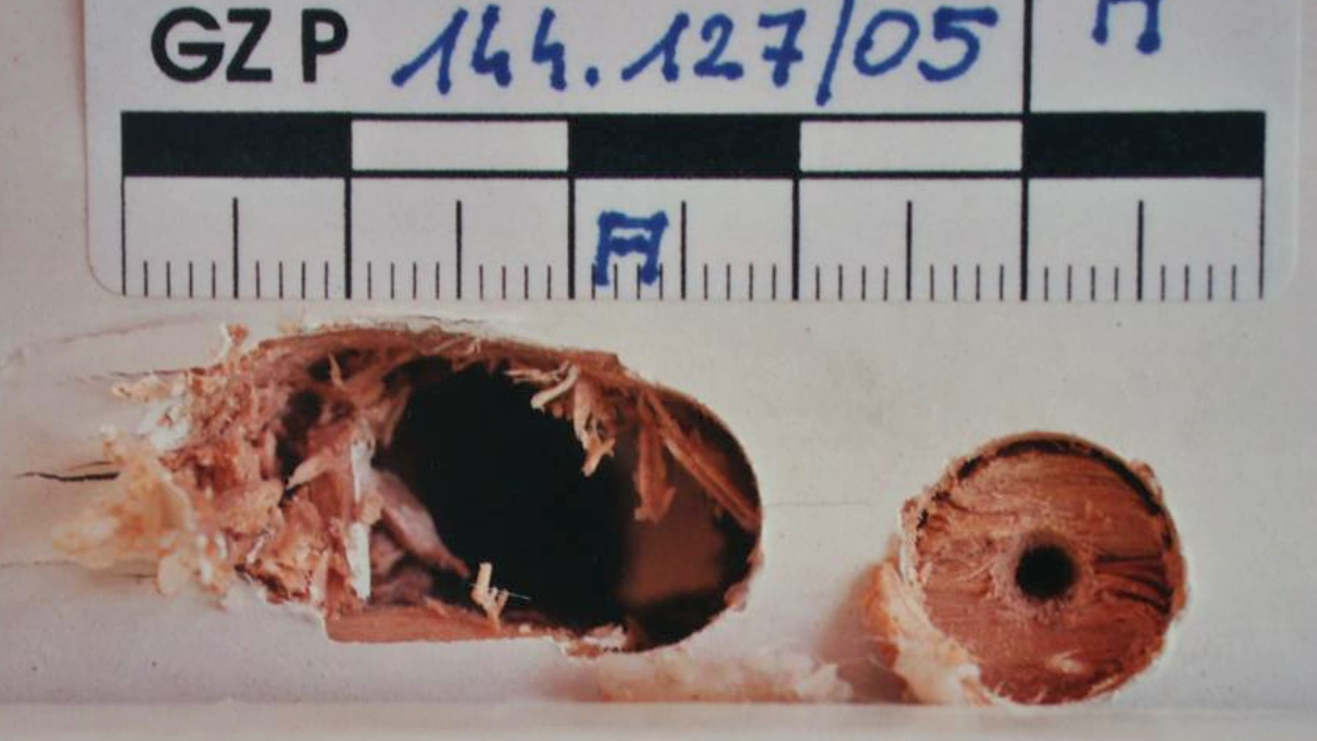 Bild aus der Polizeiakte zeigt von Einbrecher gebohrte Löcher in einem Holz-Fensterrahmen. Erkennunsgsdienstliche Markierungen am Bildrand. Schrifteinblendung "Polizeifoto" oben rechts.