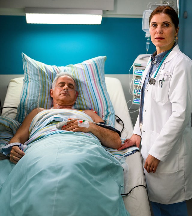 "Bettys Diagnose - Einbrüche": Prof. Dr. Alexander von Arnstett (Florian Fitz) liegt mit geschlossenen Augen im Krankenbett. Ein Sauerstoffschlauch führt in seine Nase. Neben seinem Bett steht Dr. Nadira Abbas (Yasmina Djaballah), die besorgt in die Ferne schaut.