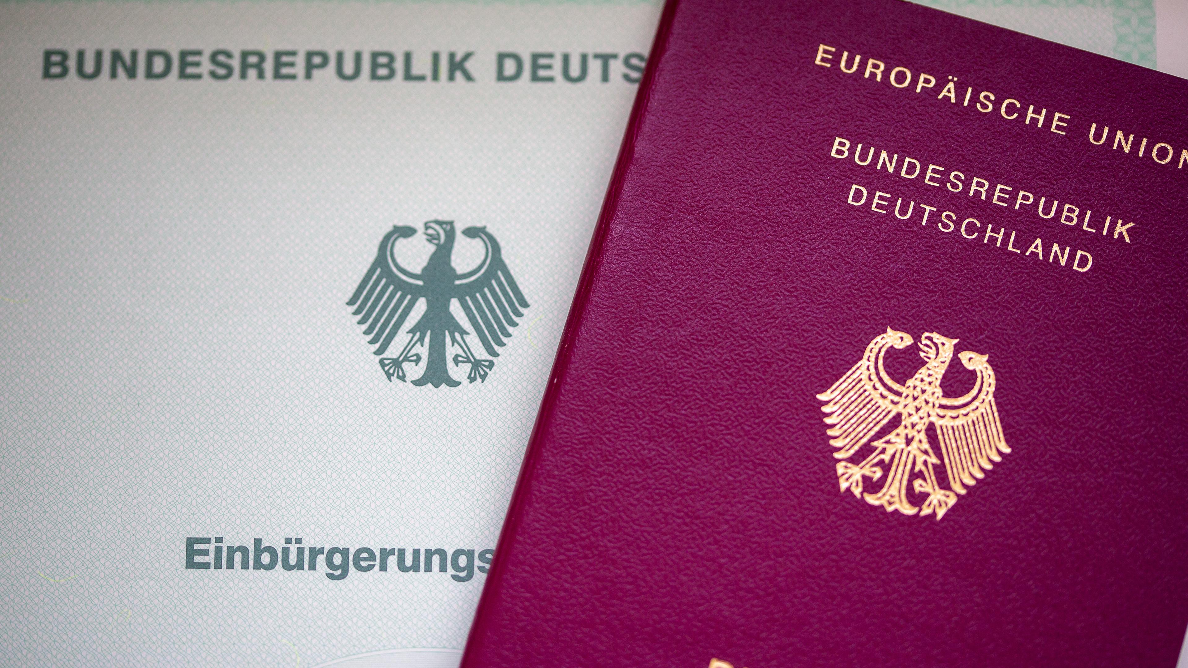 22.05.2023, Berlin: Eine Einbürgerungsurkunde der Bundesrepublik Deutschland (l) und ein deutscher Reisepass liegen auf einem Tisch.