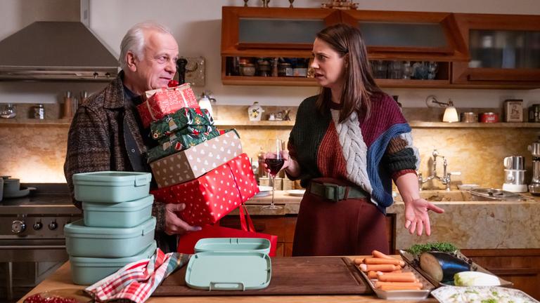 In der Küche der Familie Schott: Links vom Tresen steht Bernie (Bernhard Schütz) bis unters Kinn mit einem Stapel Geschenke beladen. Bittend schaut er seine Tochter Silja (Bettina Burchard) an, die vor ihm steht und fassungslos auf das von ihm vorbereitete Weihnachtsmenü deutet.