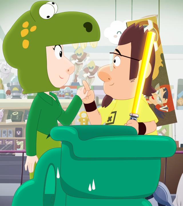 Kenny (rechts) und eine Frau im Dino-Kostüm (links) stehen sich in Kennys Spielzeugladen gegenüber und halten lächelnd Händchen.