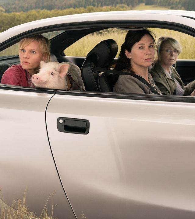 "Eine ganz heiße Nummer 2.0": Waltraud (Gisela Schneeberger), Maria (Bettina Mittendorfer) und Lena (Rosalie Thomass) sitzen im Auto. Waldtraud ist am Steuer, während Lena auf dem Rücksitz ein Schweinchen auf dem Schoß hat. Alle schauen mit fragendem Blick aus dem Fenster.