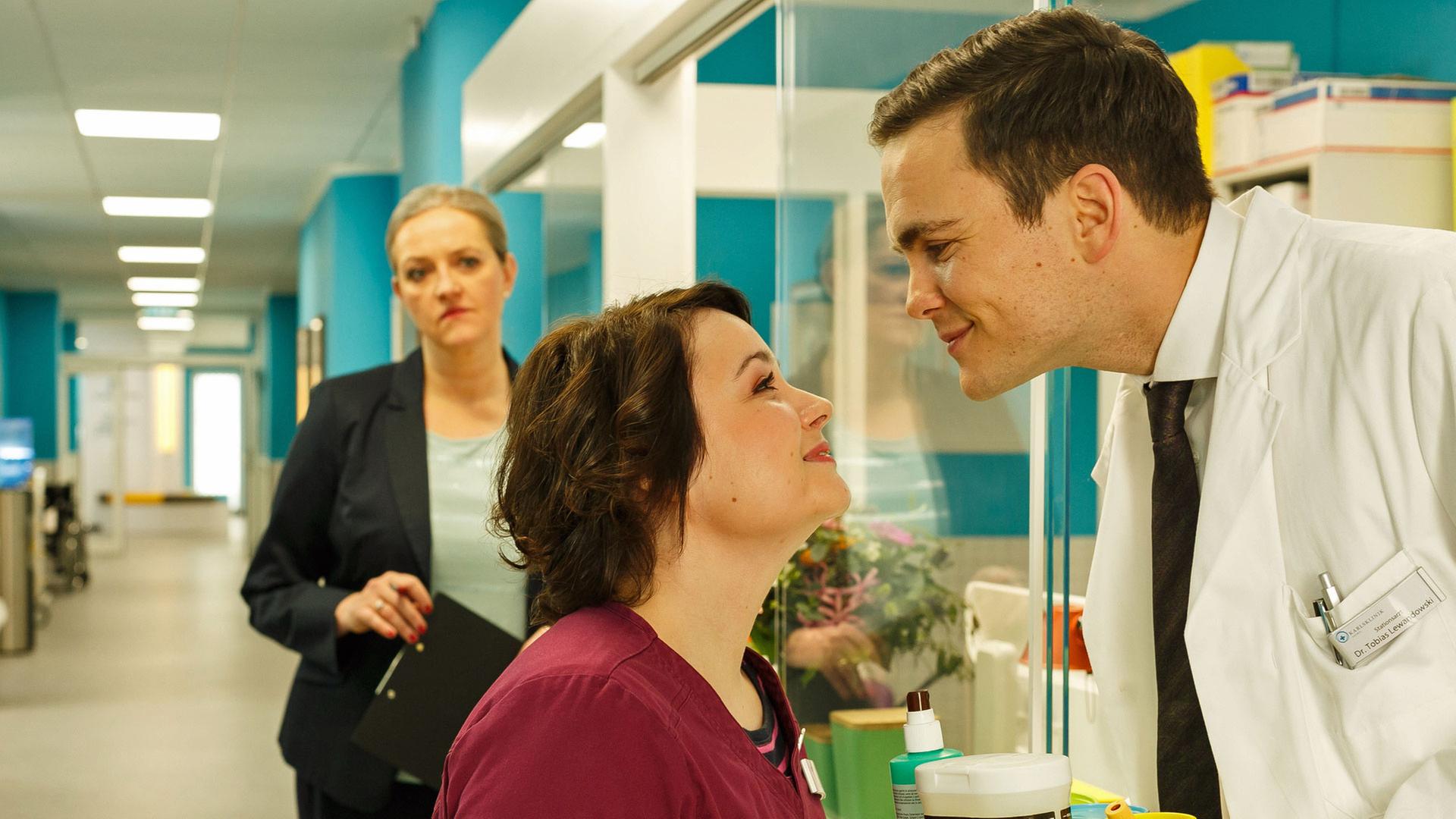 "Bettys Diagnose - Eine Kleinigkeit zu viel": Frau Mechthild Puhl (Sybille J. Schedwill) beobachtet die Turtelei während der Arbeitszeit zwischen Schwester Talula Pfeifer (Carolin Walter) und Dr. Tobias Lewandowski (Eric Klotzsch).