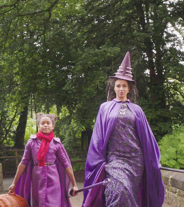Edith, die neue Schülerin mit ihren prominenten Eltern in lilanen Hexenumhängen und Hexenhüten.