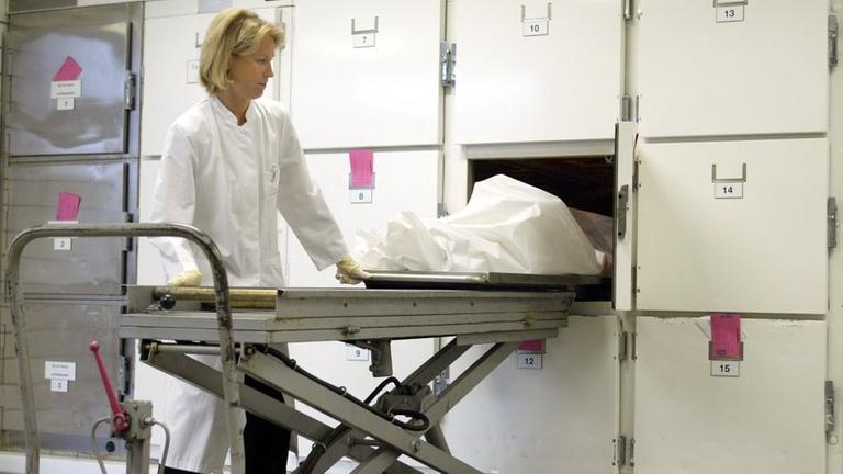 Eine Rechtsmedizinerin zieht eine Leiche aus der Kühlbox