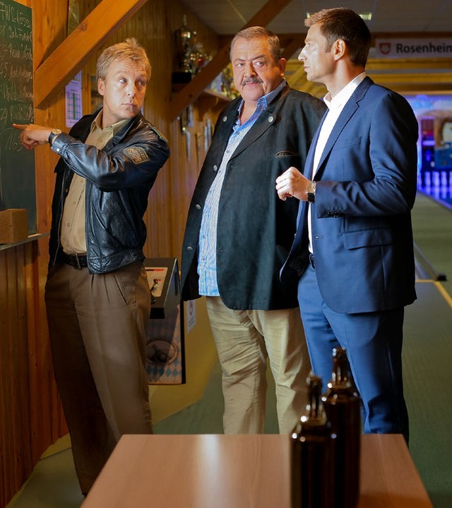 "Die Rosenheim-Cops - Einen auf einen Streich": Neben der Kegelbahn, an der Tafel des letzten Spiels, stehen die Kommissare Hofer (Joseph Hannesschläger), Kollege Hansen (Igor Jeftić) und Polizist Mohr (Max Müller).