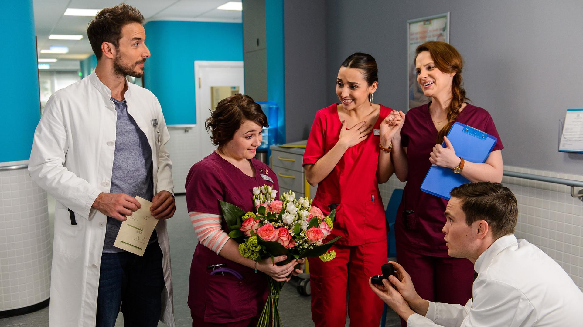 "Bettys Diagnose - Einer für den anderen": Dr. Tobias Lewandowski (Eric Klotzsch) macht Talula Pfeifer (Carolin Walter) vor den Augen der Kollegen Dr. Frank Stern (Max Alberti), Ava Edemir (Rona Özkan) und Hanna Winter (Marie Zielcke) einen Heiratsantrag.