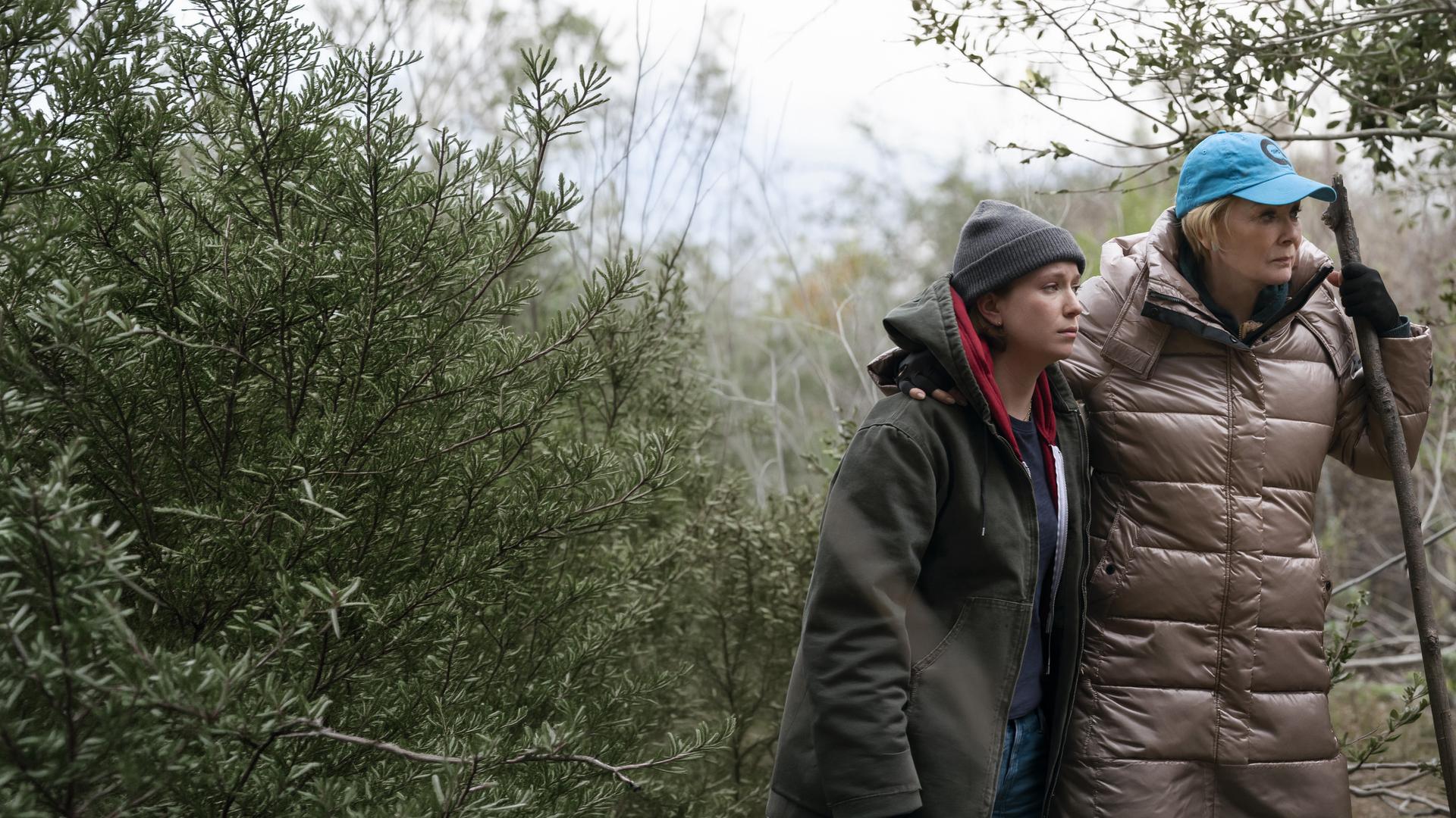 "Hacks - Eines Tages ist jetzt": Deborah und Ava stehen in Outdoorkleidung nebeneinander. Deborah hält in ihrer Hand einen großen Stock, auf den sie sich zu stützt. Um sie herum stehen Bäume und Sträucher.