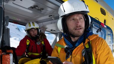 Katharina (Luise Bähr) sitzt im Hubschrauber. Markus (Sebastian Ströbel) steht daneben und hält ein Mobiltelefon in der Hand.