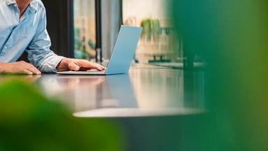 Ein Geschäftsmann lächelnd an einem Tisch hinter seinem Laptop