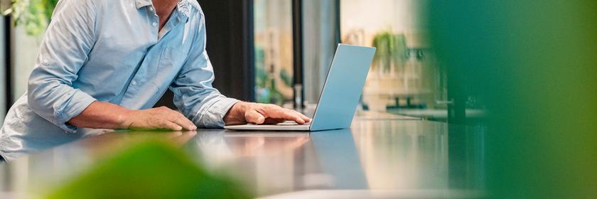 Ein Geschäftsmann lächelnd an einem Tisch hinter seinem Laptop