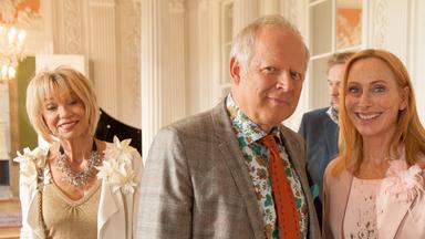 Gundula (Andrea Sawatzki) und Gerald (Axel Milberg) schauen strahlend in die Kamera. Im Hintergrund ist der Rest der Familie zu sehen.