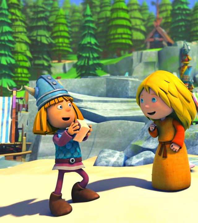 Wickie steht auf einem Platz im Dorf, er hat ein Stück Seife in der Hand. Ilvy steht rechts neben ihm. Beide sehen fröhlich aus.