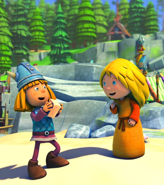 Wickie steht auf einem Platz im Dorf, er hat ein Stück Seife in der Hand. Ilvy steht rechts neben ihm. Beide sehen fröhlich aus.