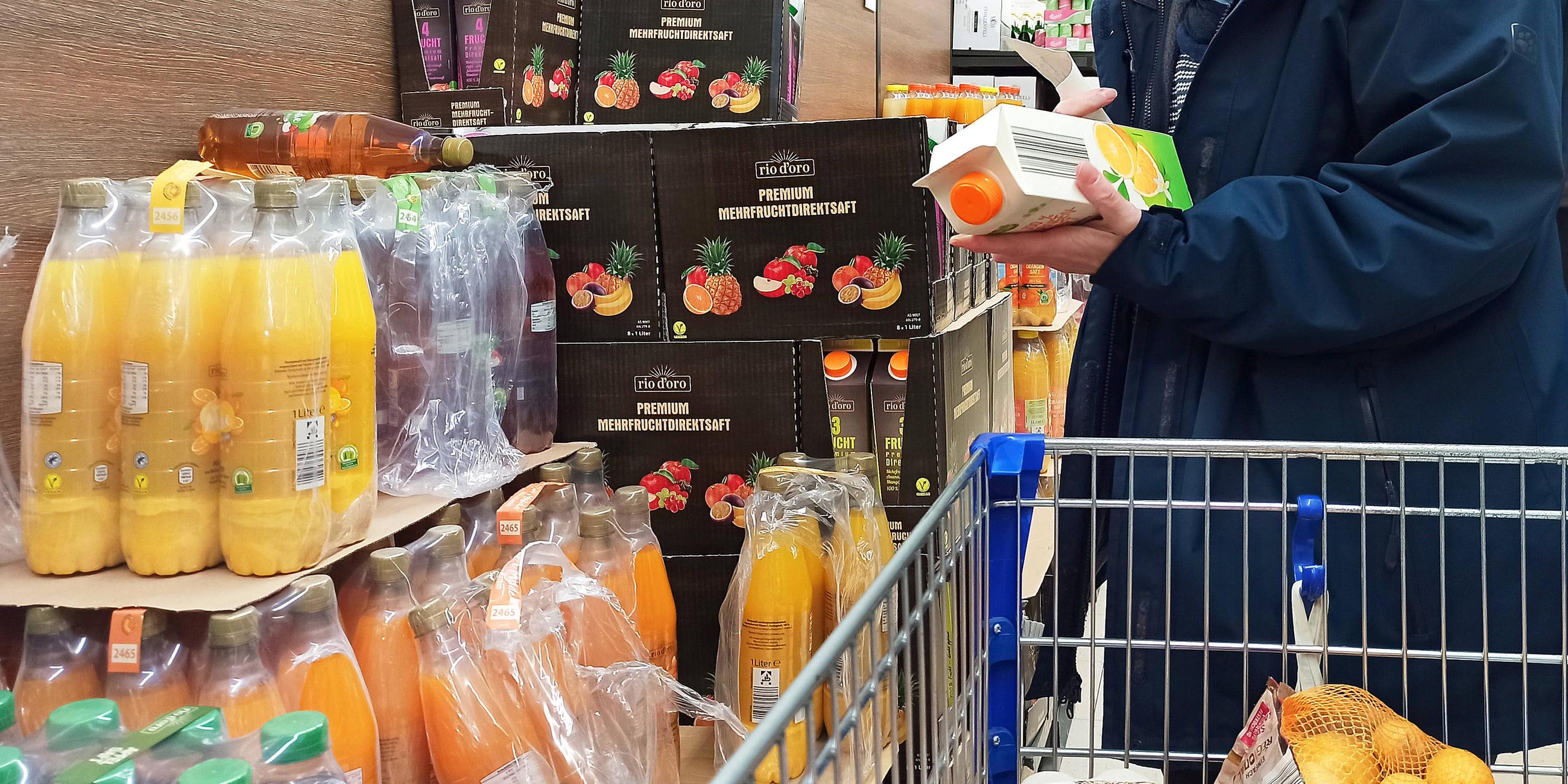 Eine Frau mit Einkaufswagen schaut auf eine Pachkung von Orangensaft im Supermarkt
